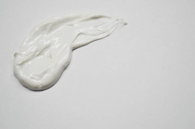 Beyaz arka planda lekelenmiş beyaz krema damlası.