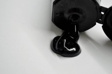 Siyah kozmetik ürünü olan açık tüp beyaz arka planda yatıyor.