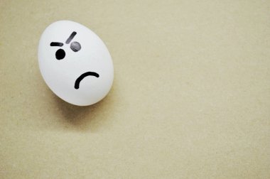 Ahşap arka planda kızgın yüzü boyanmış beyaz yumurta..