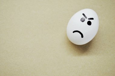 Ahşap arka planda kızgın yüzü boyanmış beyaz yumurta..