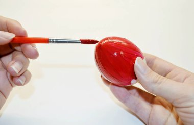 Kadının eli bir yumurtayı fırçayla kırmızıya boyuyor..