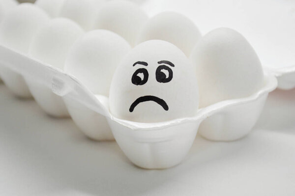 Белое яйцо с раскрашенным грустным лицом в подносе.