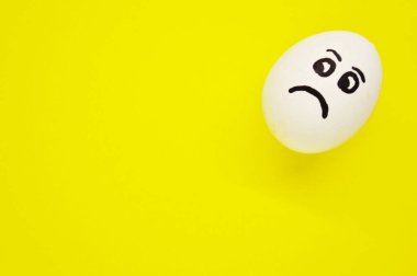 Sarı arka planda üzgün yüzü boyanmış beyaz yumurta..