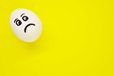Sarı arka planda üzgün yüzü boyanmış beyaz yumurta..