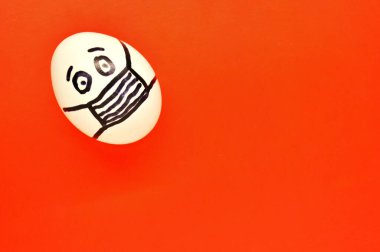 Kırmızı arka planda maske takan yüzü boyalı beyaz bir yumurta..