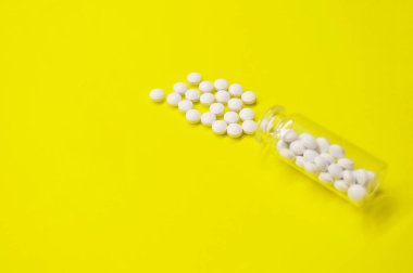 Sarı arka planda fotokopi alanı olan beyaz haplar ve şişe, Sağlıklı ve Tıp Konsepti.