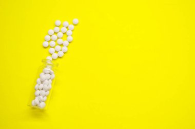 Sarı arka planda fotokopi alanı olan beyaz haplar ve şişe, Sağlıklı ve Tıp Konsepti.