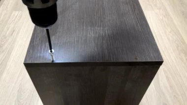 Adam, tahtadaki vidaları sıkmak için tornavida kullanıyor. Adam bir dolabın iki tahtasını sürgüler ve perçin takar.