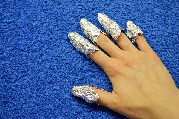 Removing shellac from nails. fingers with foil on a blue background. Close-up hand. Front view.