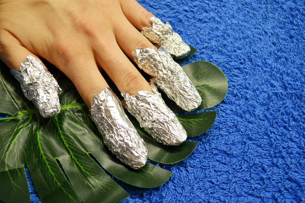 Removing shellac from nails.fingers with foil on leaf of palm on blue background — Stock Photo, Image