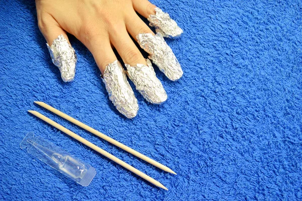 Tırnaklarından Shellac çıkarılıyor. Mavi arka planda folyolu, serumlu ve turuncu çubuklu parmaklar. Yakından çek. Ön görünüm.