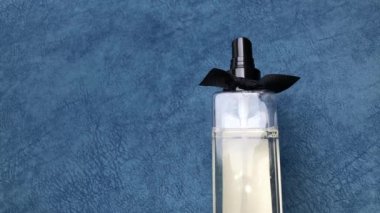 Kadın eli parfüm serpiyor. Mavi arka planda işaret parmağına basıyor..