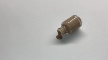 Glass jar with beige nail polish lies on a white background and flows.