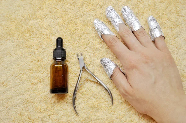 Fingers with foil, glass bottle with a pipette and wire cutters on beige towel — Stock Photo, Image