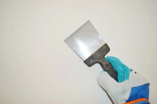 Mavi iş bezi eldiveni beyaz duvar arka planına karşı bir spatula tutar.