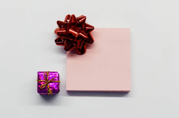 红色的闪光弓作为礼物 粉色的闪光小礼物作为白底便条放在纸上 — 图库照片