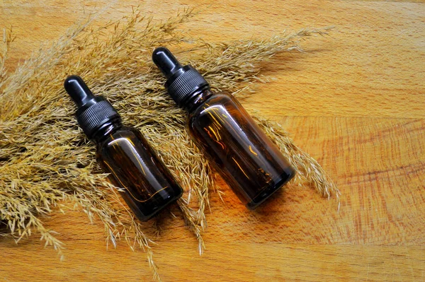 Brown glass bottles with a pipette lie on fluffy dry grass on wooden background — Stock Photo, Image