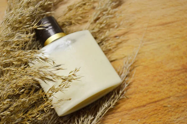 Flasche mit beigem Gel liegt auf flauschigem, trockenem Gras auf hölzernem Hintergrund — Stockfoto