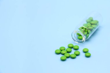 Yeşil kabuklu tabletler, mavi arka plandaki cam şişeden dökülmüş. İlaç üretimi ve ambalajı. Sağlıklı bir yaşam için vitaminler. Yukarıdan manzara. Dümdüz. Kopyalama alanı.