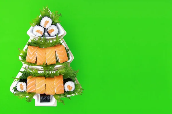 Noel 'de suşi konsepti. Yeşil zemin üzerinde beyaz bir tabakta suşi. Japon restoranı için yaratıcı bir fikir. Düz. Tepeden manzara. Kopyalama alanı.
