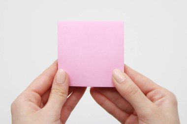 A pair of hands of a young girl holding a clean, clean, pink sheet of paper for notes and reminders with an adhesive base or sticker on a light background, close-up. Empty space for design and text.Location