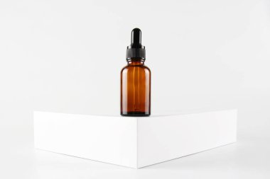 Beyaz bir podyum ve beyaz bir zemin üzerinde kahverengi camdan yapılmış boş bir cam damlatıcının maketi. Cilt bakım serumu, pankart ya da şablon. Doğal kozmetik ürünleri konsepti..