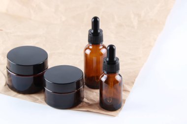 Kraft kağıdının arka planında camdan yapılmış boş bir cam damlalık şişesi ve krema kavanozu. Serum, cilt bakım kremi, pankart ya da şablon. Doğal kozmetik ürünleri konsepti..