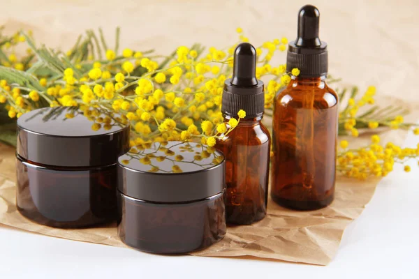 Clean cosmetic bottles with mimosa flowers, stand on craft paper on a white background.Empty label packaging for the brand layout.The concept of spring natural cosmetics, a banner of a cosmetic sale.