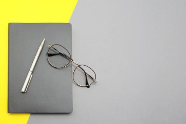 Gri bir not defteri, kalem ve şık gözlükler gri-sarı bir arka plana yerleştirilir. İş adamları, eğitim, teknoloji konsepti, üst görüş için eşyalar. 2021 'in renkleri gri ve sarıdır.