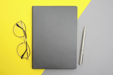 Gri bir not defteri, kalem ve şık gözlükler gri-sarı bir arka plana yerleştirilir. İş adamları, eğitim, teknoloji konsepti, üst görüş için eşyalar. 2021 'in renkleri gri ve sarıdır.