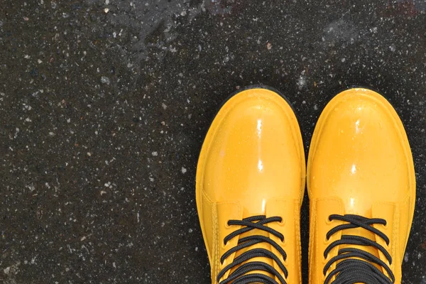 Yellow rain boots stand in a large puddle on the asphalt after the rain.Women\'s stylish autumn boots.The concept of the sale of the autumn collection of shoes, discounts, promotions.Top view.Copyspace