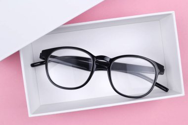 Siyah çerçeveli optik gözlük pembe bir arka planda beyaz bir hediye kutusunda. İndirim, promosyon, optik mağazalarda satış, gözlüklerin onarımı, gözlüklerin hediye olarak onarımı.