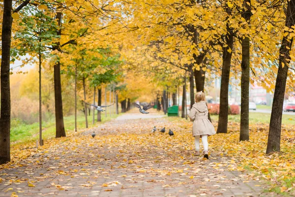 Beautiful little girl runs for birds in autumn park — Stock Photo, Image