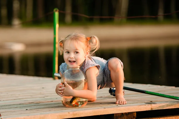 Criança feliz com um peixe que ele pegou ao lado de uma lagoa Fotos De Bancos De Imagens