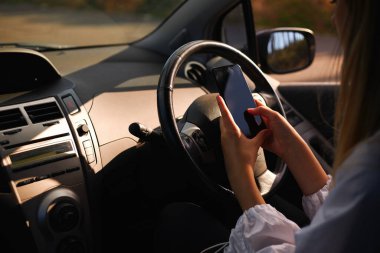 Araba kullanırken cep telefonuyla mesajlaşan ve yola konsantre olmayan genç bir kadının görüntüsünü kapat.