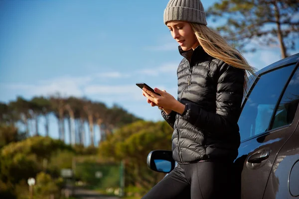 Young woman standing next to car which has broken down or she could be lost and trying to get signal on mobile phone to use map app or call for help