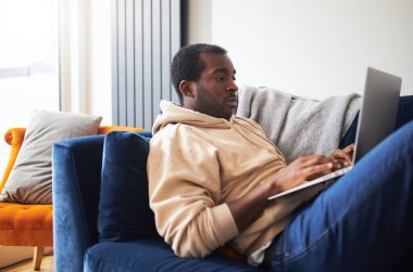 Evde kanepede yatıp bilgisayarla internetten ya da evden çalışan melez bir gencin profil görüntüsü