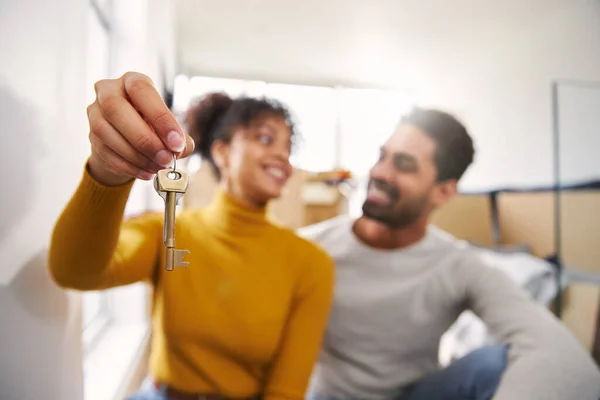 Happy Couple In Lounge Of New Home Holding Keys On Moving Day Surrounded By Removal Boxes