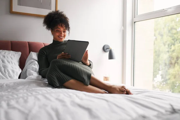 Evdeki yatakta dinlenen kadın dijital tablette TV programı okuyor ya da yayınlıyor.