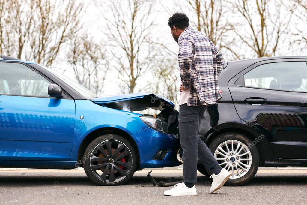 Young man looking at damaged car hit from behind after traffic accident