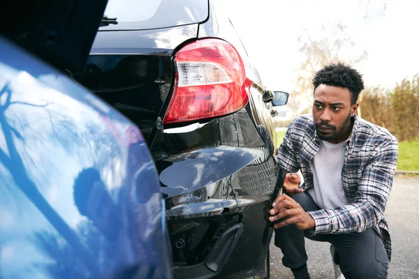 車の公園で車を破壊されたことによって立って怒っている若い男は 携帯電話を使用して保険会社への損傷を報告 — ストック写真