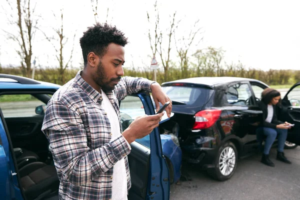 交通事故の後に破損した車で立っている若い男携帯電話を使用して保険会社に事件を報告 — ストック写真