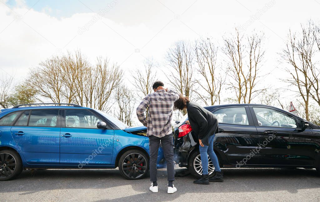 Young male and female drivers looking at damaged car hit from behind after traffic accident