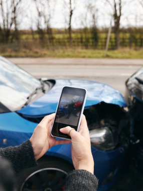 Kadın sürücünün sigorta talebi için cep telefonuyla trafik kazasının fotoğraflarını çekerken yakın plan.