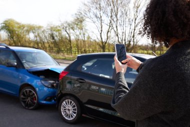 Kadın sürücünün sigorta talebi için cep telefonuyla trafik kazasının fotoğraflarını çekerken arkadan görüntüsü