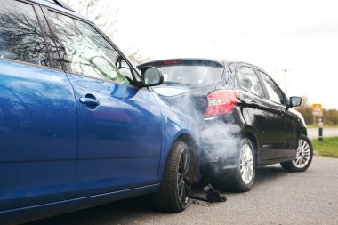 Yolun kenarında trafik kazasına karışan iki araba kaput ve çamurlukta hasar var.