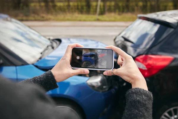 Kadın sürücünün sigorta talebi için cep telefonuyla trafik kazasının fotoğraflarını çekerken yakın plan.