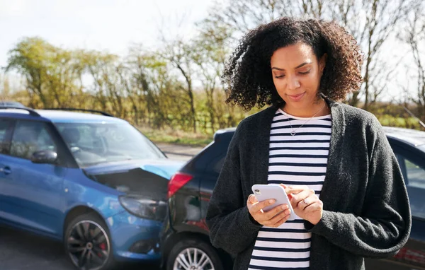 交通事故後の被害車のそばに立つ若い女性携帯電話を使用して保険会社に事故を報告 — ストック写真