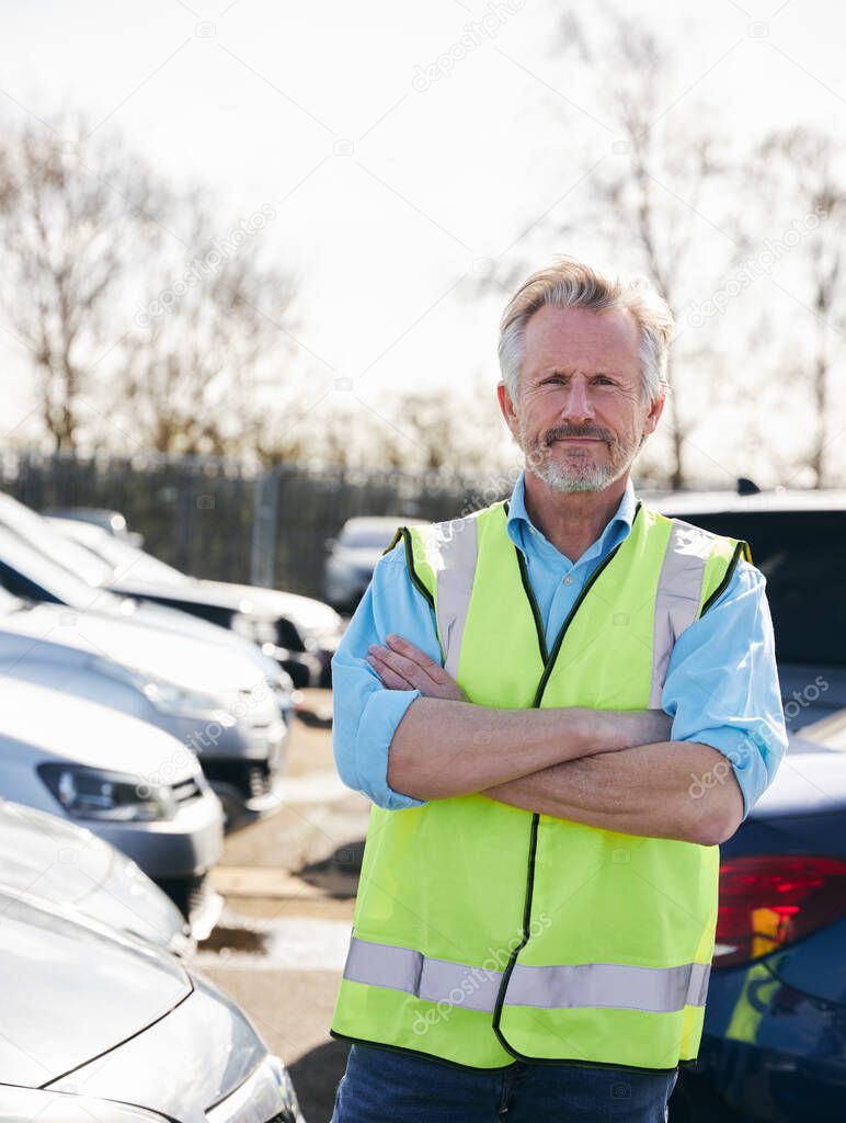Portrait of mature male car park attendant wearing hi-vis safety vest folding arms