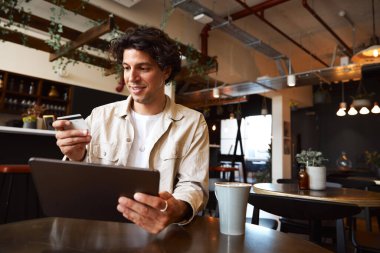 Kahve dükkanındaki genç adam kredi kartıyla online işlem yapıyor.